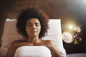 a woman relaxes on a massage table surrounded by salt scrubs, warm massage oils, soft light, and orchids